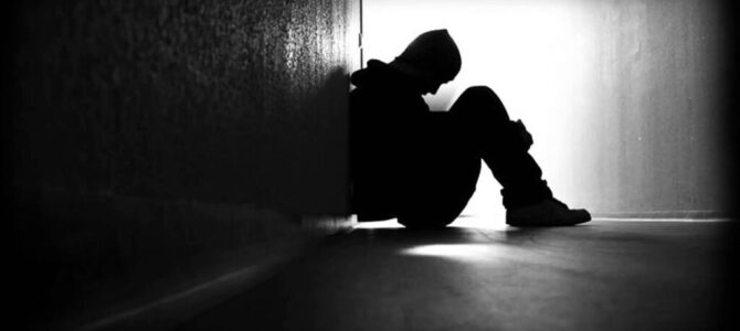 Silhouette of a man huddled in a corner of a hall looking emotional